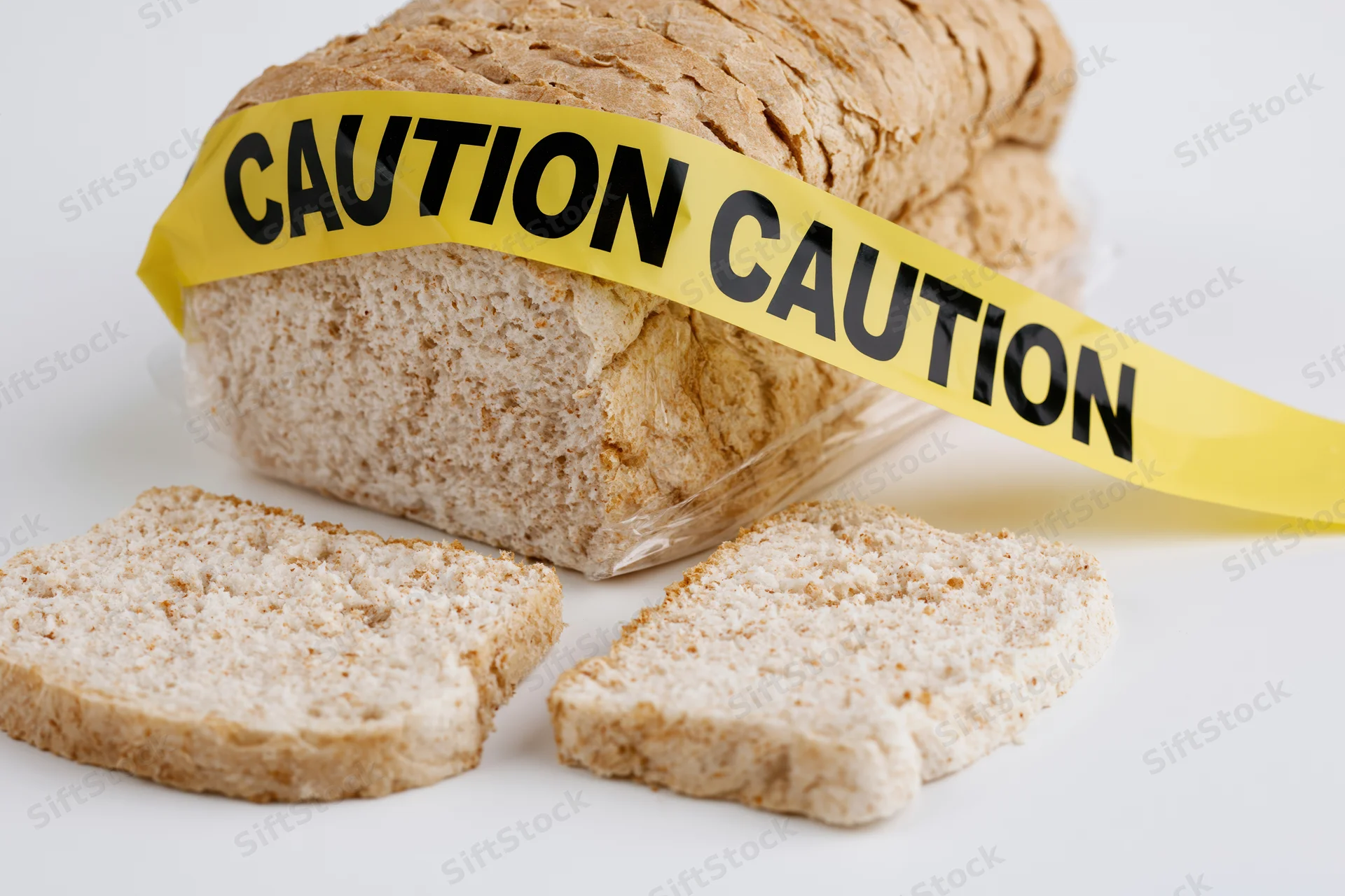 Loaf of sliced white sandwich bread wrapped in plastic with yellow caution tape across it on white background