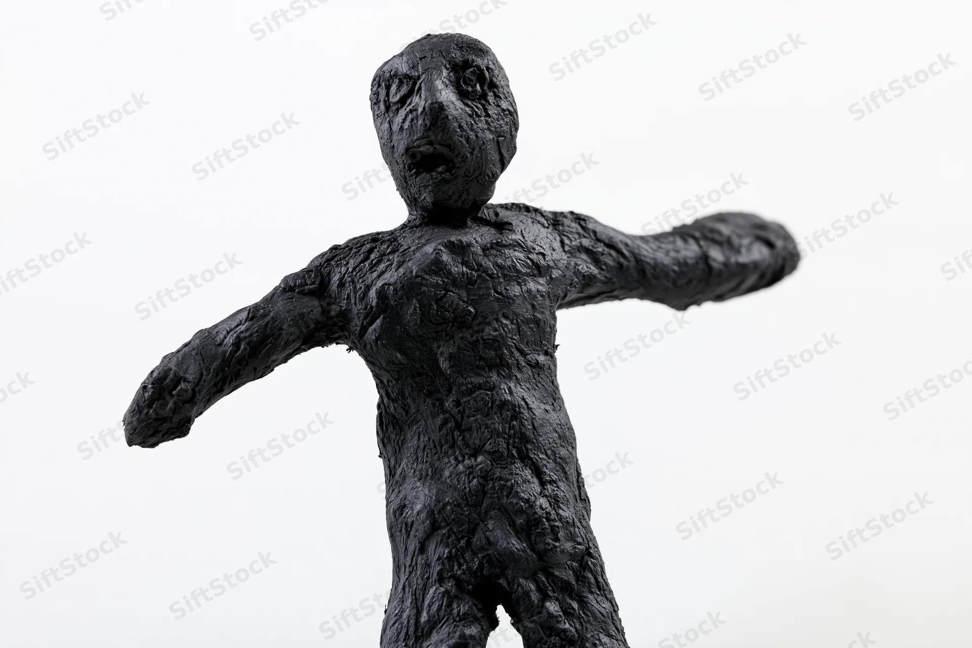Black clay sculpture of a rough humanoid figurine with arms outstretched, isolated on white background