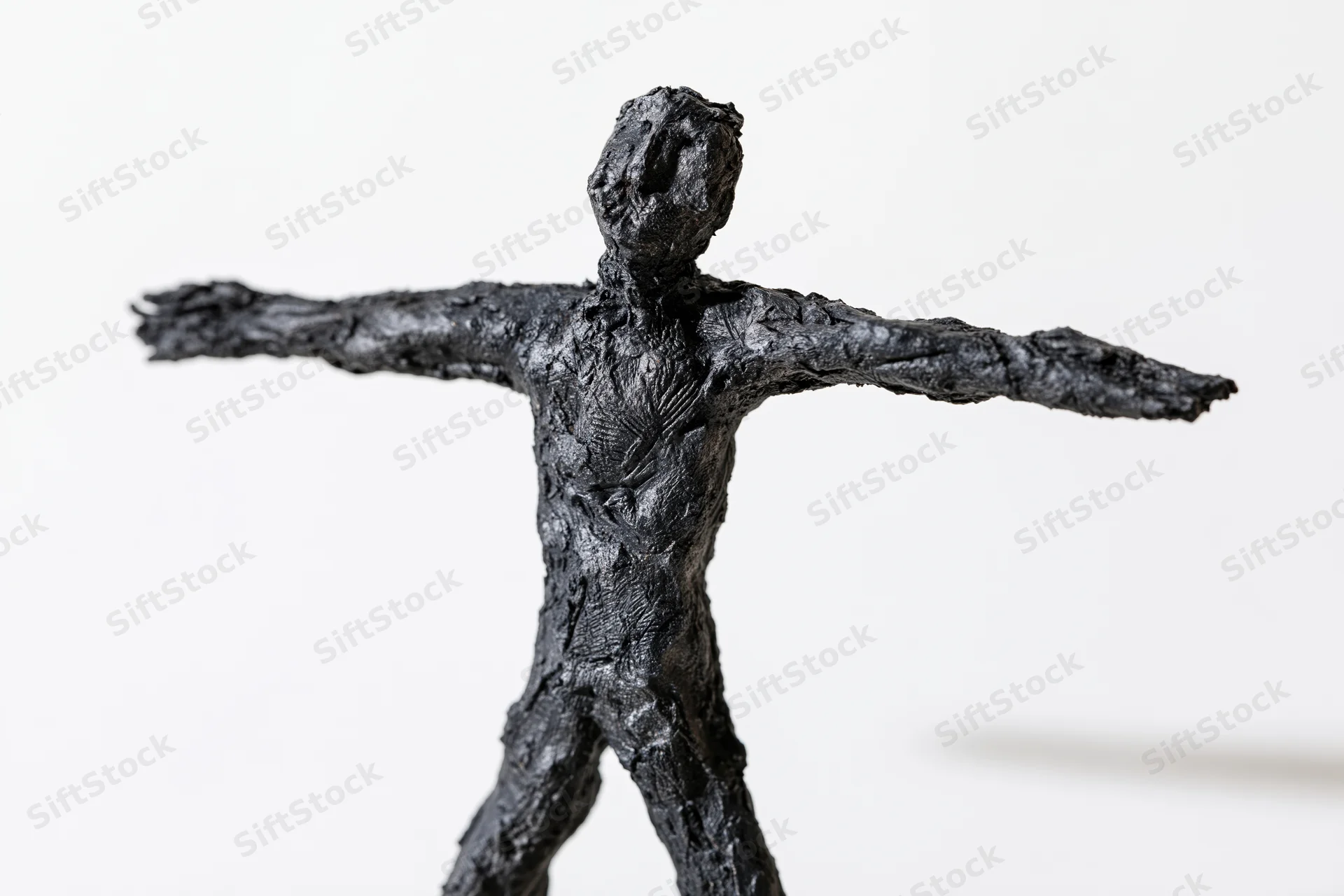 Black handmade clay sculpture of a rough humanoid figure with arms spread standing against white background
