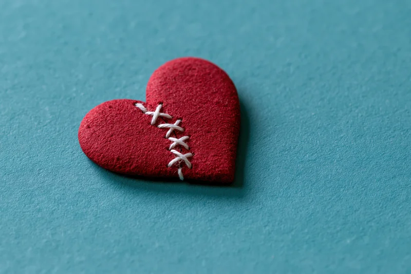 Red foam heart with white stitching across a crack on a blue textured surface