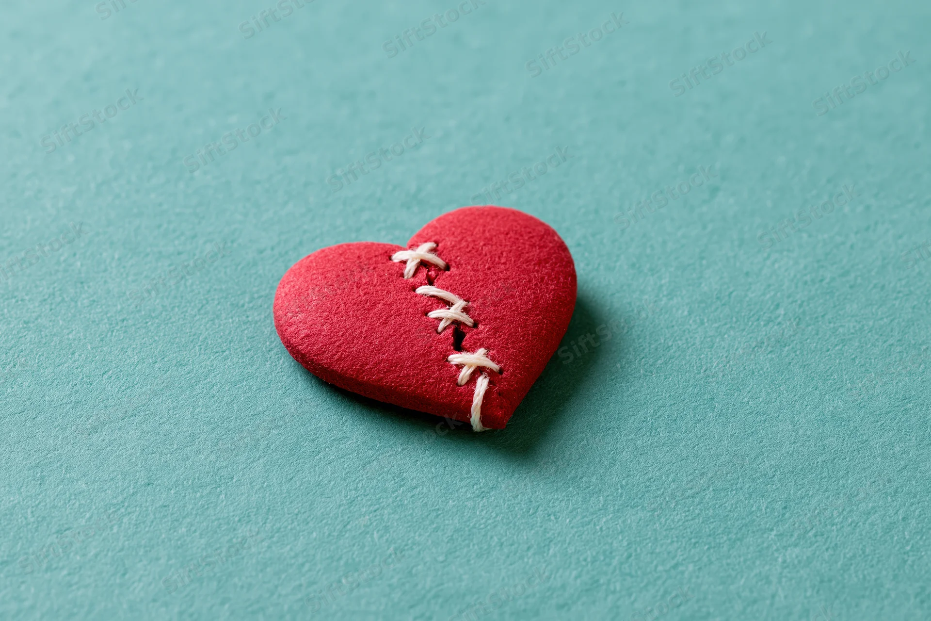 Red foam heart with white stitching across a crack resting on a turquoise surface