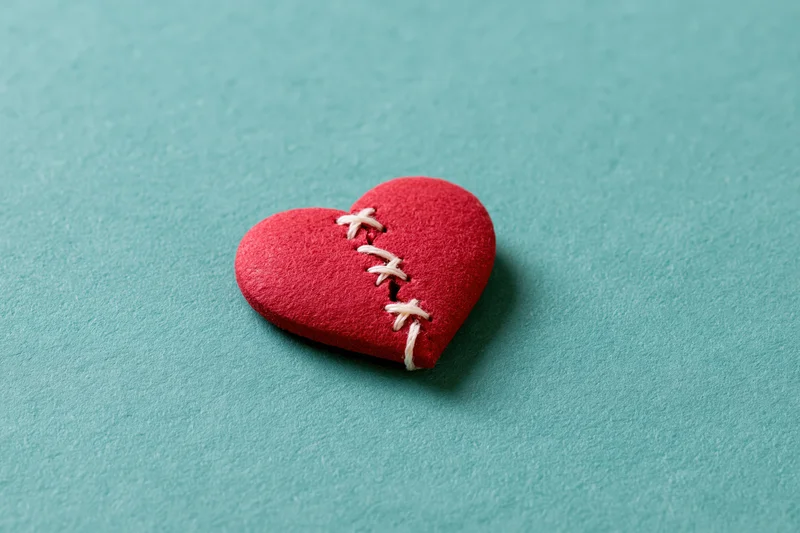 Red foam heart with white stitching across a crack resting on a turquoise surface