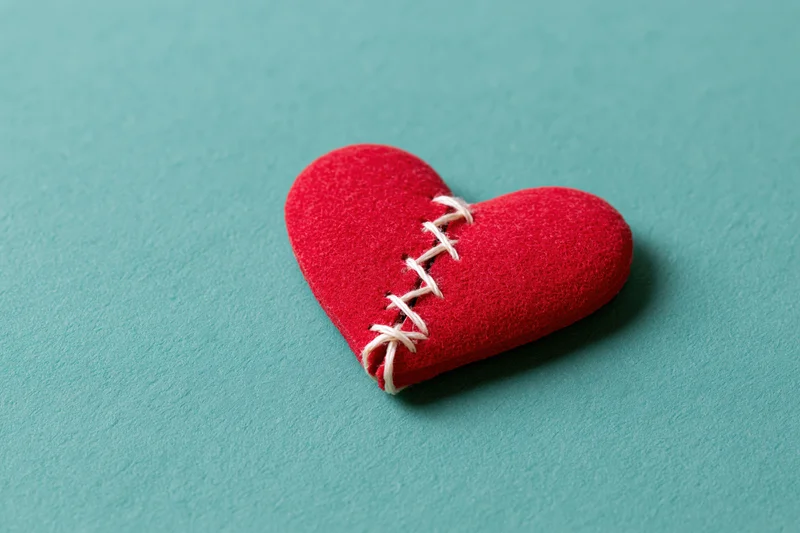 Red foam heart with white stitching across a crack on a teal surface