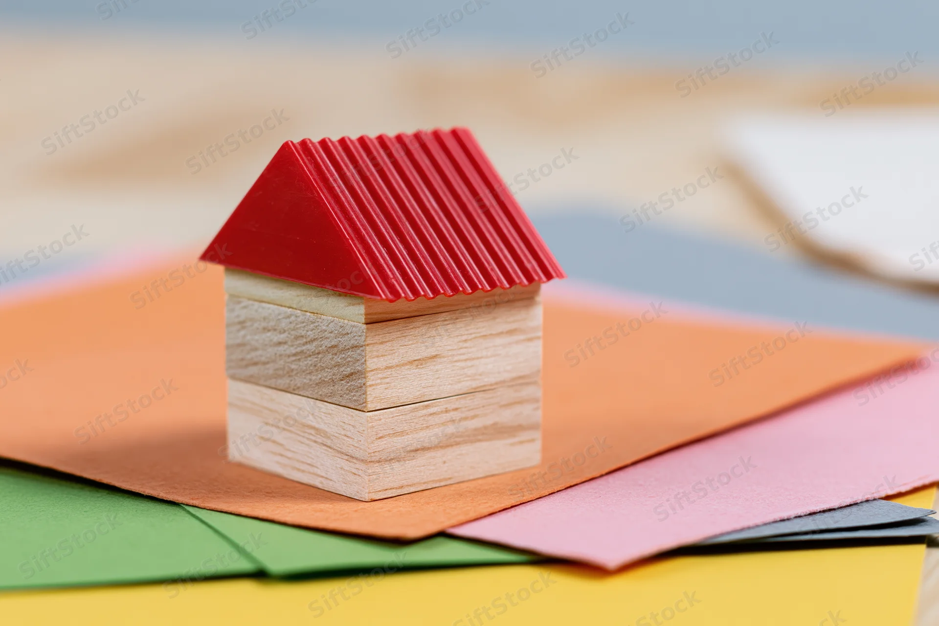 Small wooden toy house with red roof on colorful paper sheets