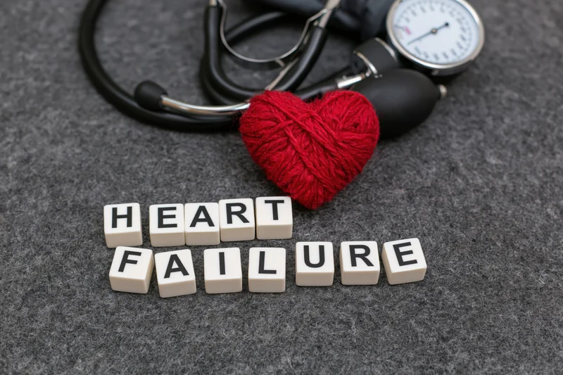 White letter cubes spelling heart failure arranged on gray surface with stethoscope and knitted red heart nearby