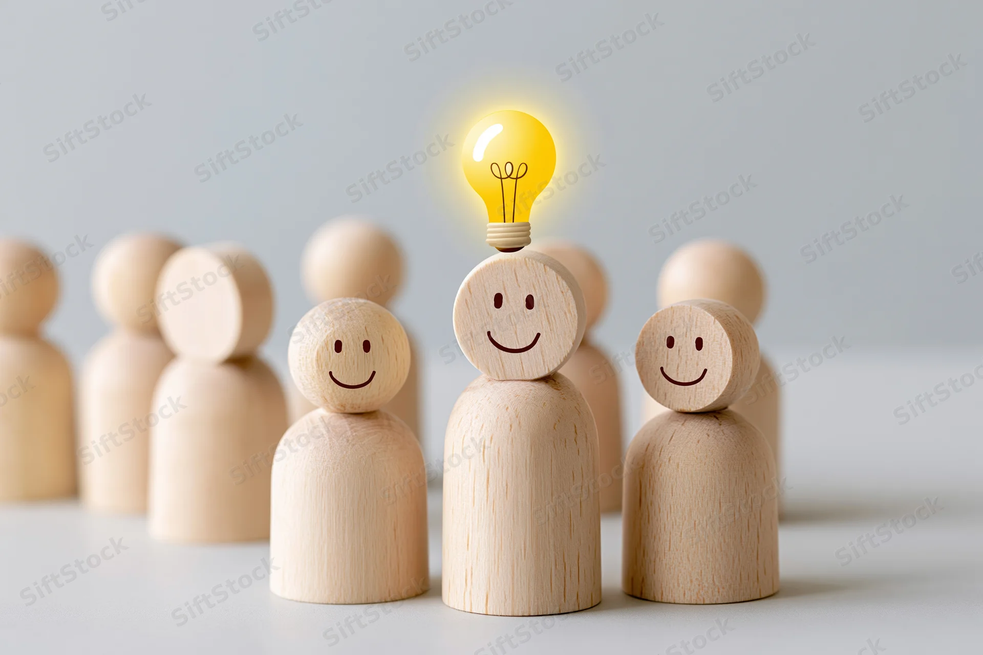 Wooden figurines in a group with one having a glowing lightbulb head, symbolizing idea generation in a team setting