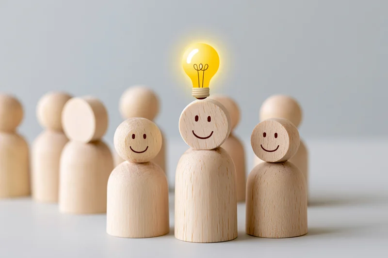 Wooden figurines in a group with one having a glowing lightbulb head, symbolizing idea generation in a team setting