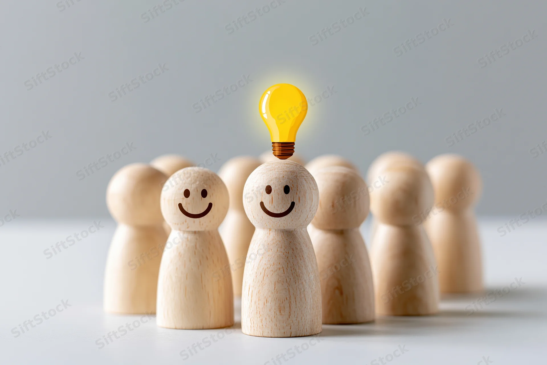 Wooden figurines in a group with one glowing lightbulb above its head on a white surface