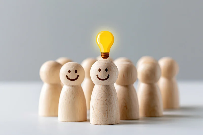 Wooden figurines in a group with one glowing lightbulb above its head on a white surface