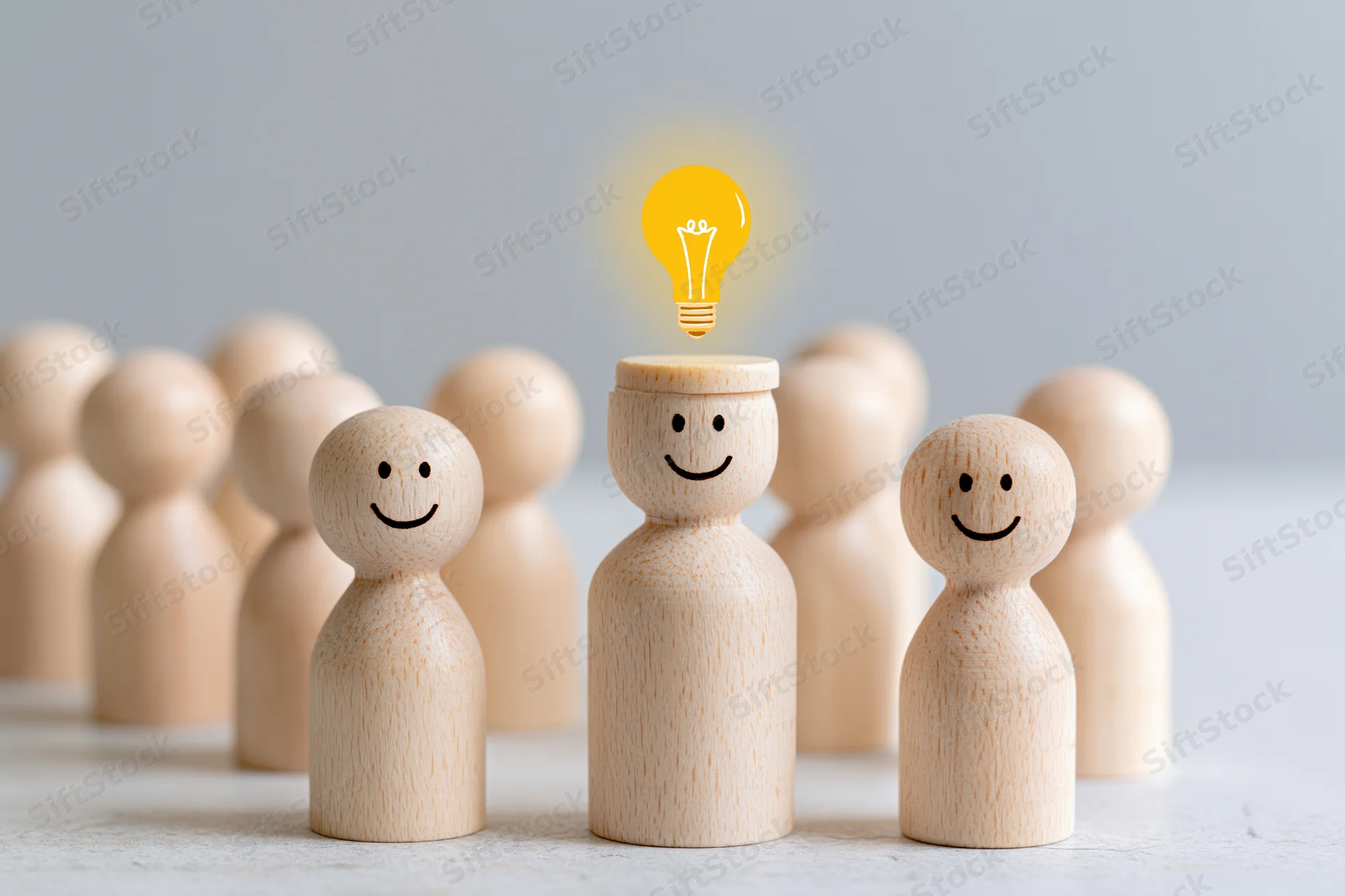 Wooden figurines in a group with one having a glowing lightbulb above its head symbolizing an idea