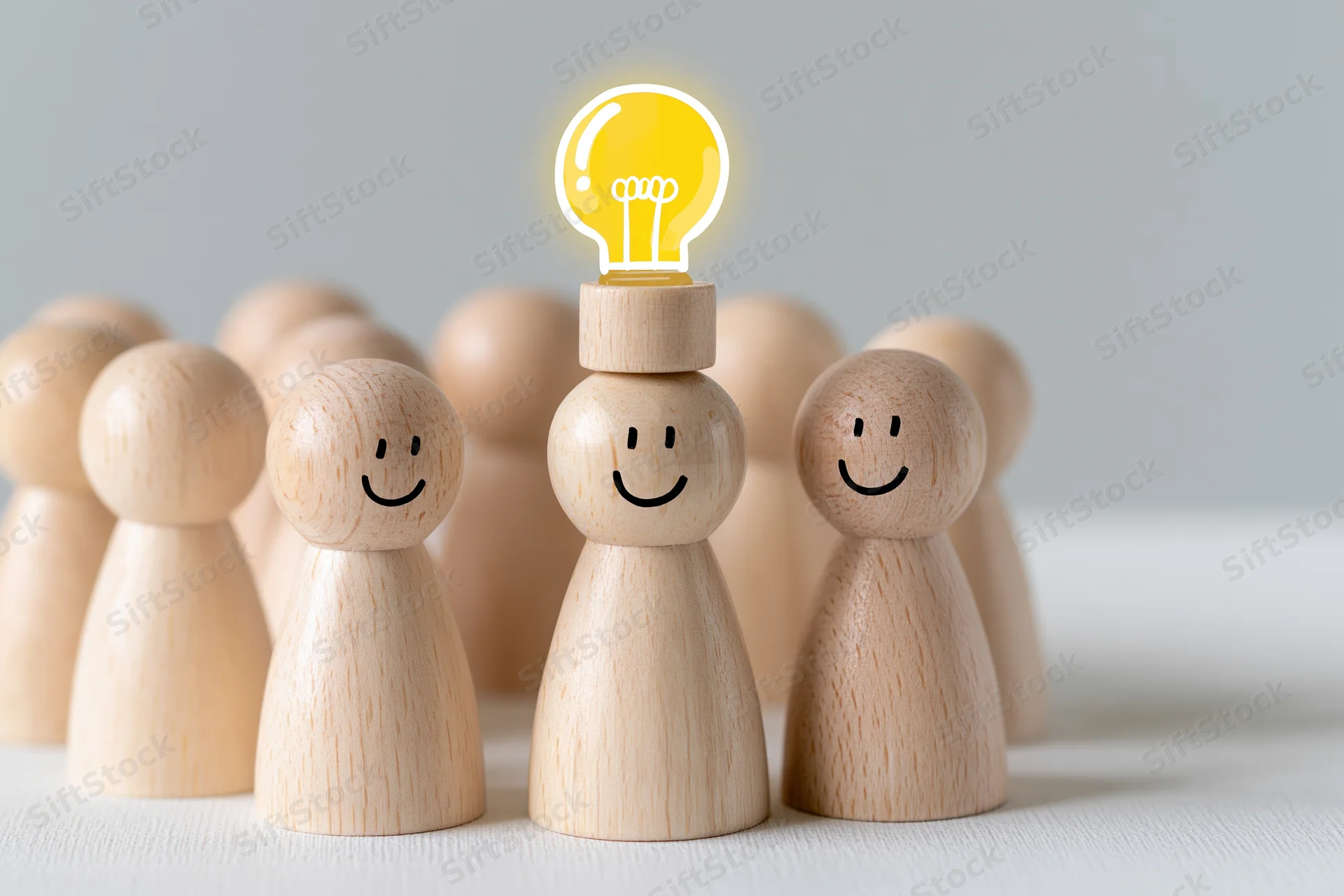 Wooden figurines in a group with one having a glowing lightbulb on its head symbolizing idea generation