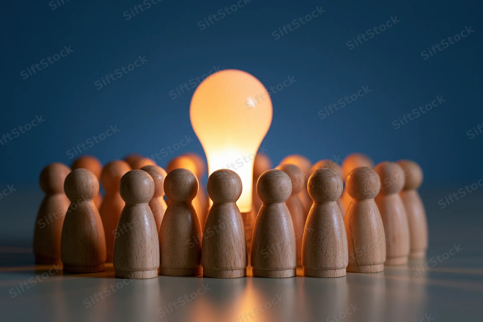 Wooden figures arranged in a circle around a glowing lightbulb on a reflective surface
