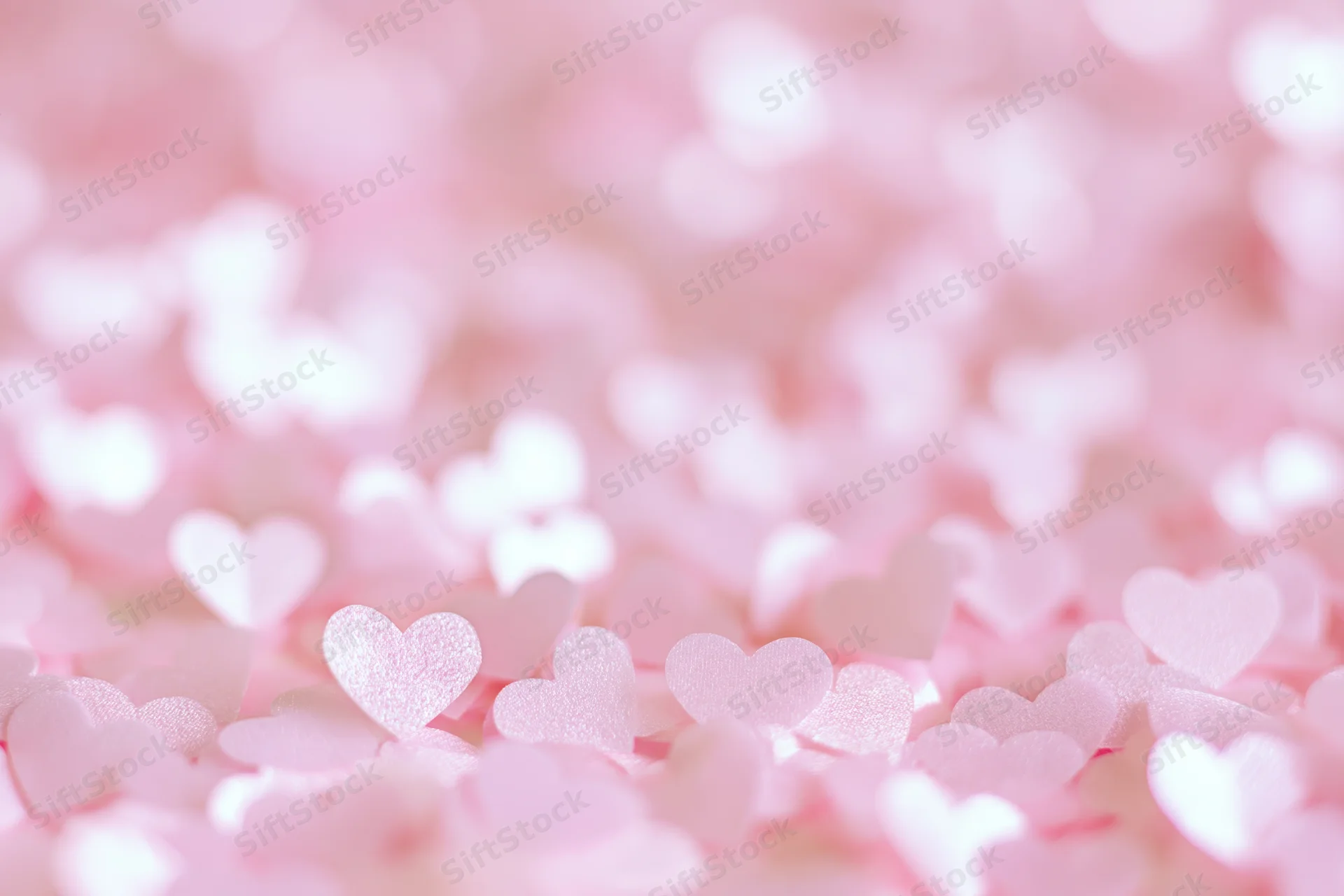 Soft pink heart-shaped confetti in shallow focus creating a bokeh background