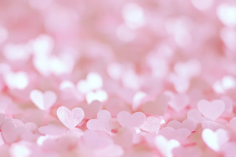 Soft pink heart-shaped confetti in shallow focus creating a bokeh background