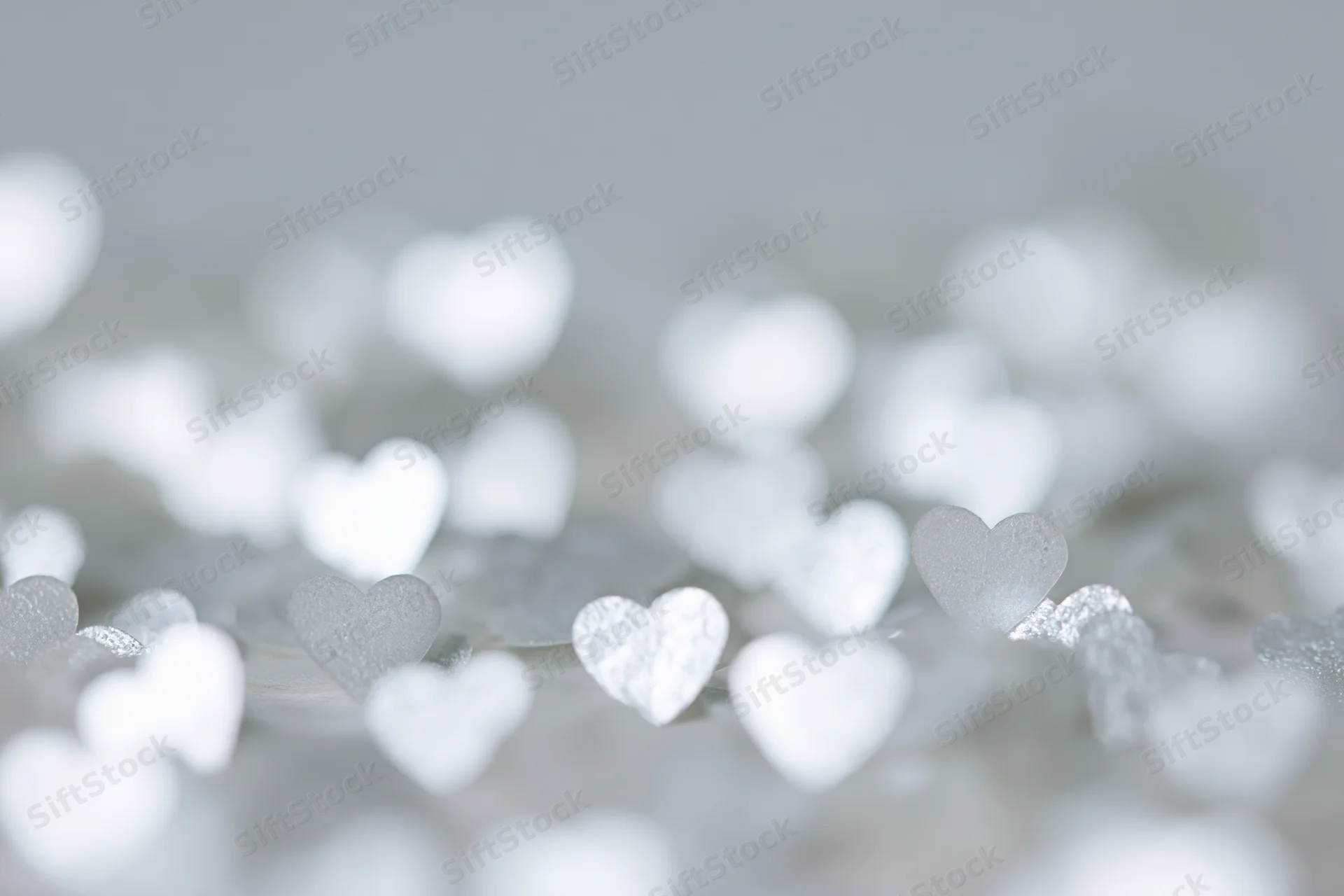 Scattered heart-shaped glitter confetti on a soft blurred white background