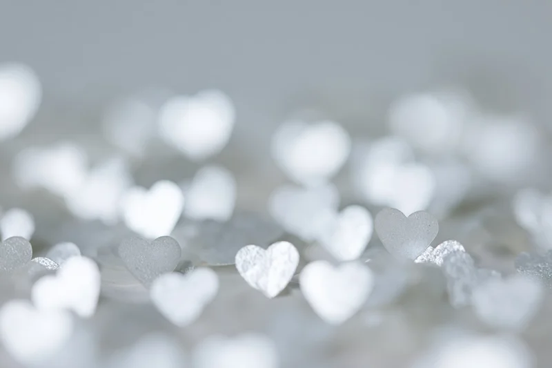 Scattered heart-shaped glitter confetti on a soft blurred white background