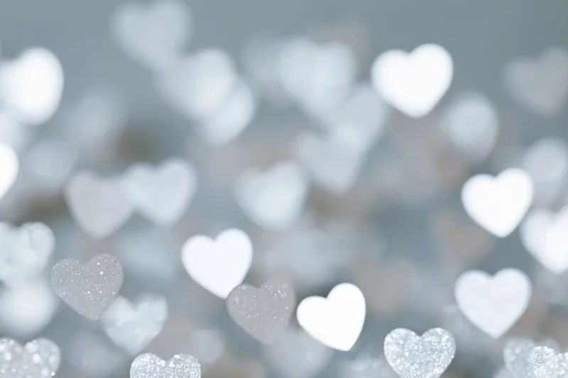 Soft bokeh background with scattered heart-shaped light spots in white and silver