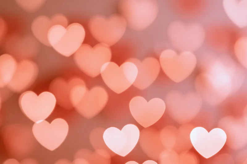 Soft out-of-focus heart-shaped bokeh lights scattered across a warm pink background