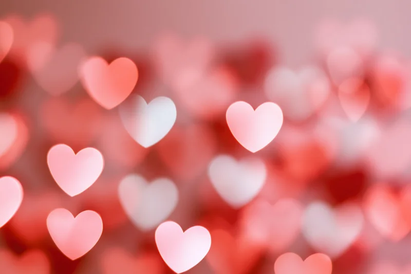 Soft out-of-focus heart-shaped bokeh lights scattered across a pink background