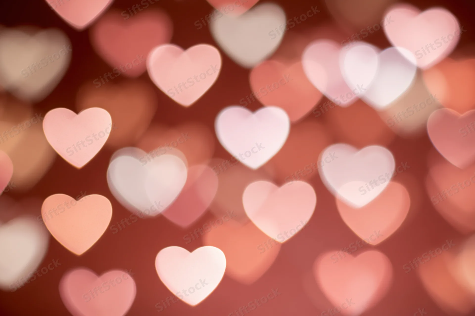 Soft out-of-focus heart-shaped bokeh lights scattered across a warm pink and red background