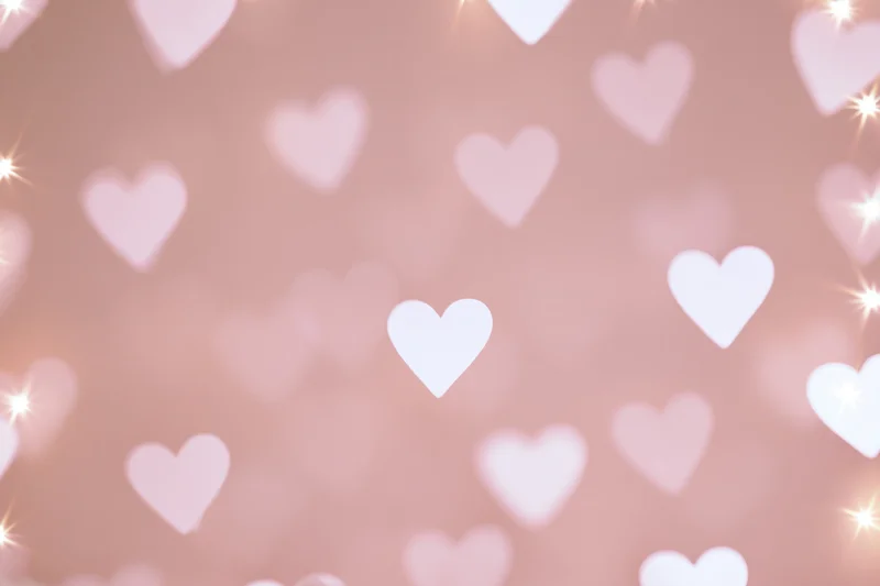 Soft pink bokeh background with scattered white heart shapes and glowing sparkles