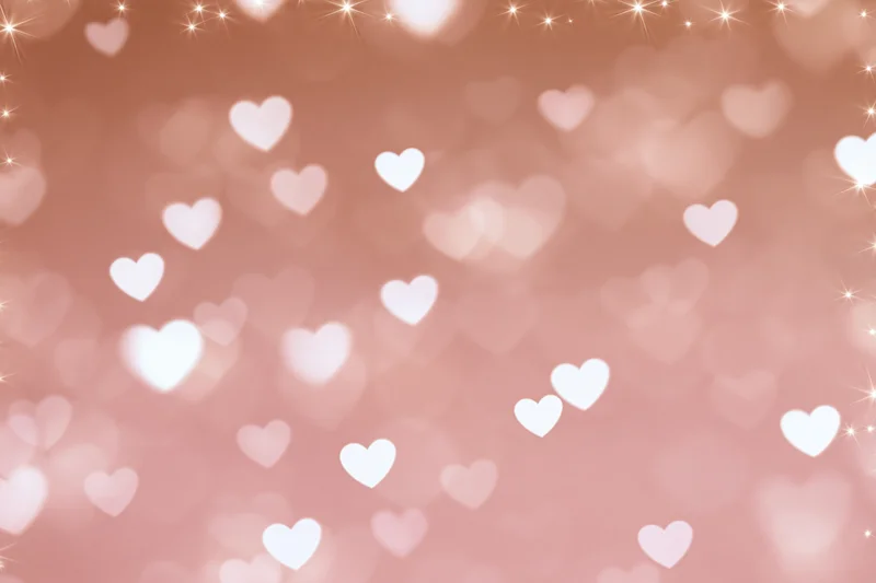 Soft pink bokeh background with scattered white heart shapes and sparkles