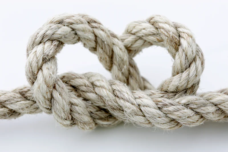 Thick natural fiber rope tied into a heart-shaped knot on white background