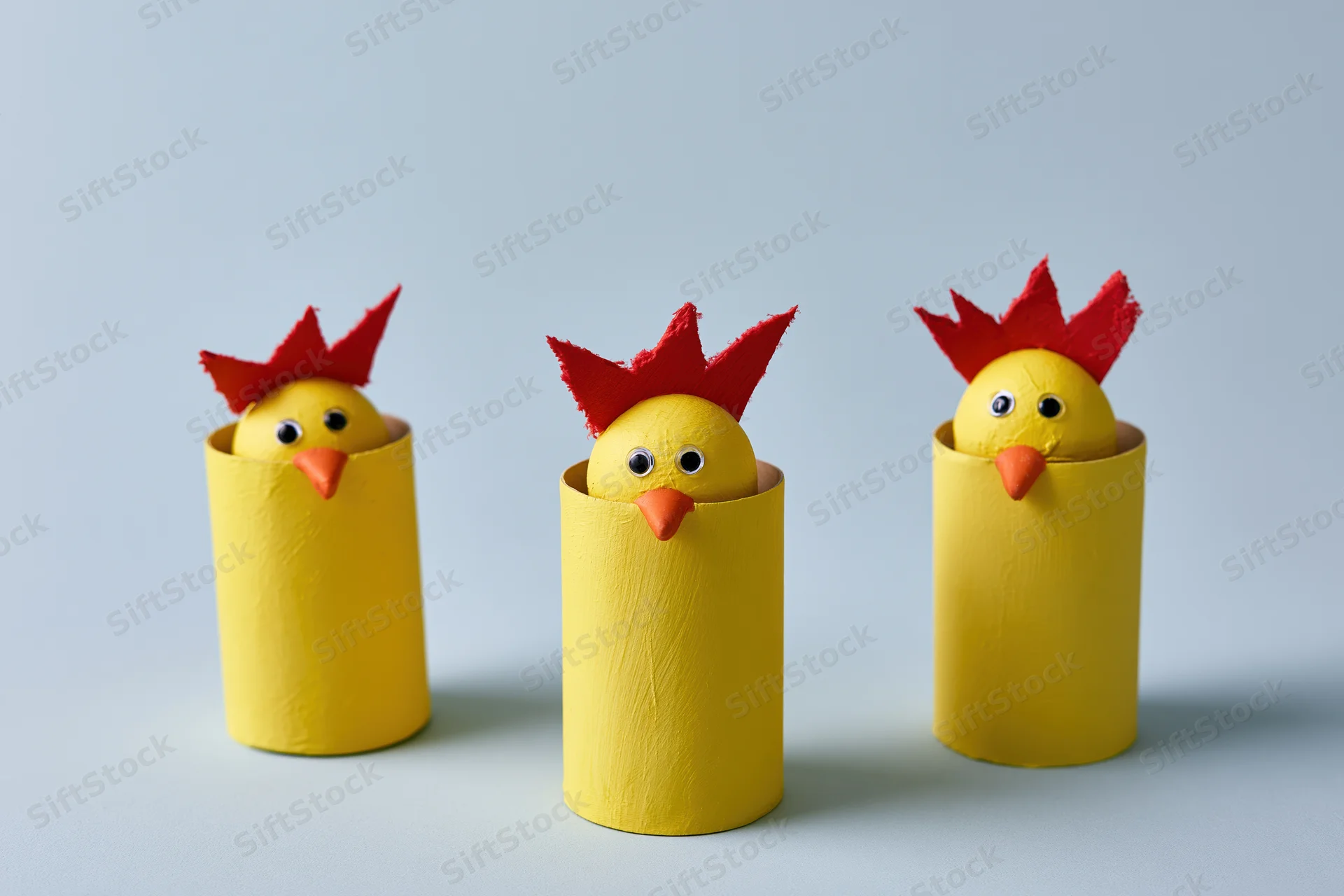 Three handmade yellow chicks with red combs peeking from cardboard tubes on a light background