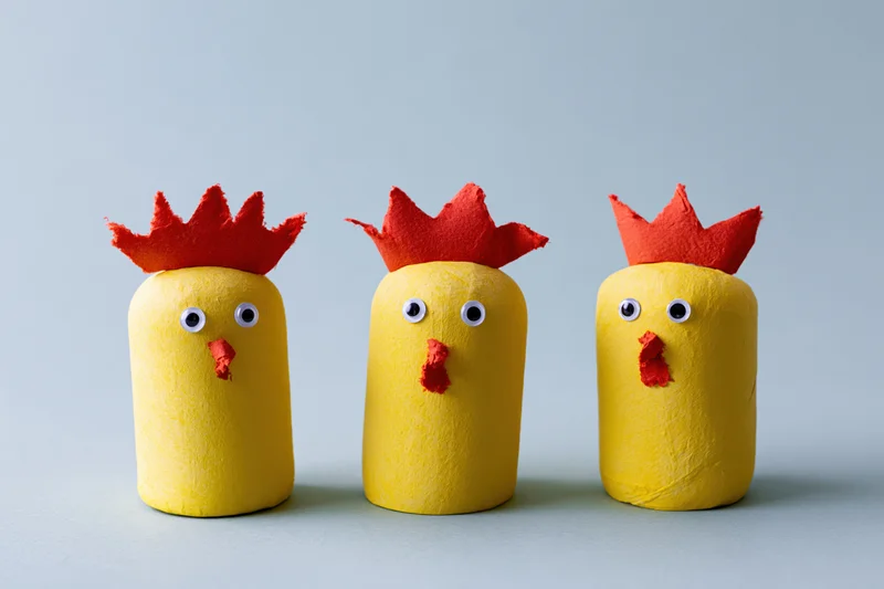 Three handmade yellow chicks with red crowns and beaks arranged in a row on a plain surface