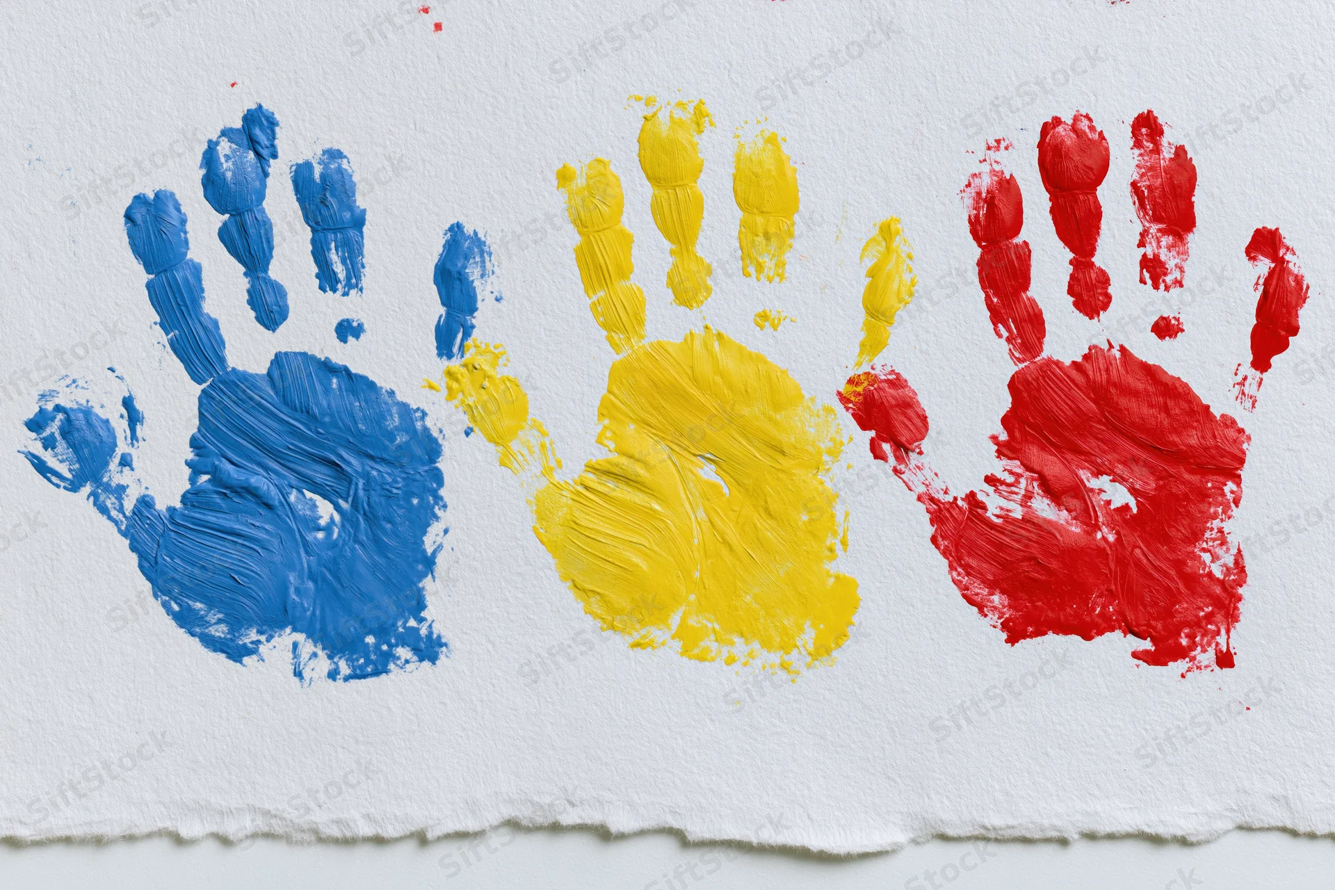 Three painted handprints in blue, yellow and red arranged side by side on white paper