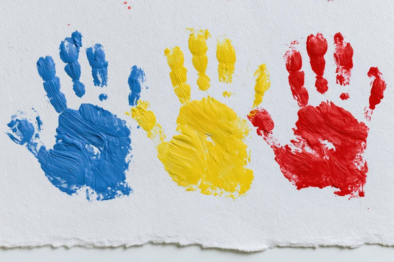 Three painted handprints in blue, yellow and red arranged side by side on white paper