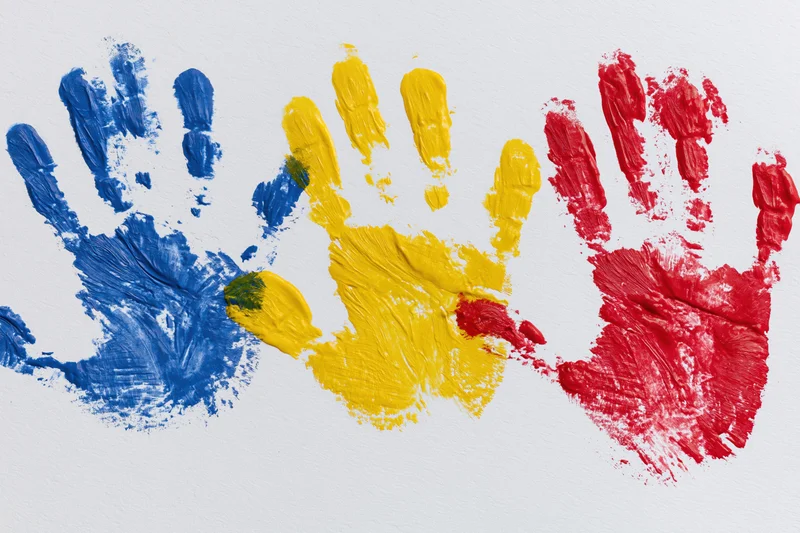 Three painted handprints in blue, yellow and red arranged side by side on white paper