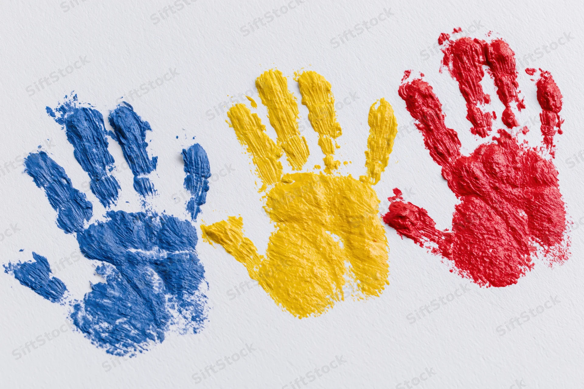 Three painted handprints in blue, yellow and red arranged side by side on white paper
