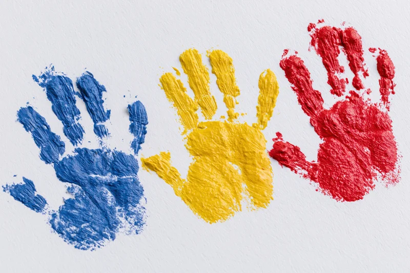 Three painted handprints in blue, yellow and red arranged side by side on white paper