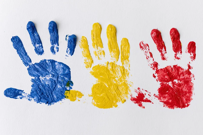Three painted handprints in blue, yellow and red arranged side by side on white paper