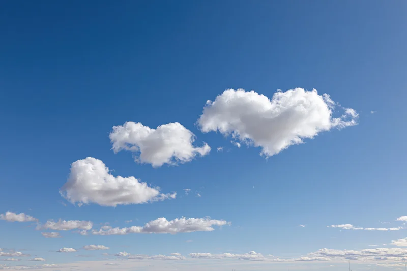 Three white fluffy clouds shaped like hearts floating in a clear blue sky