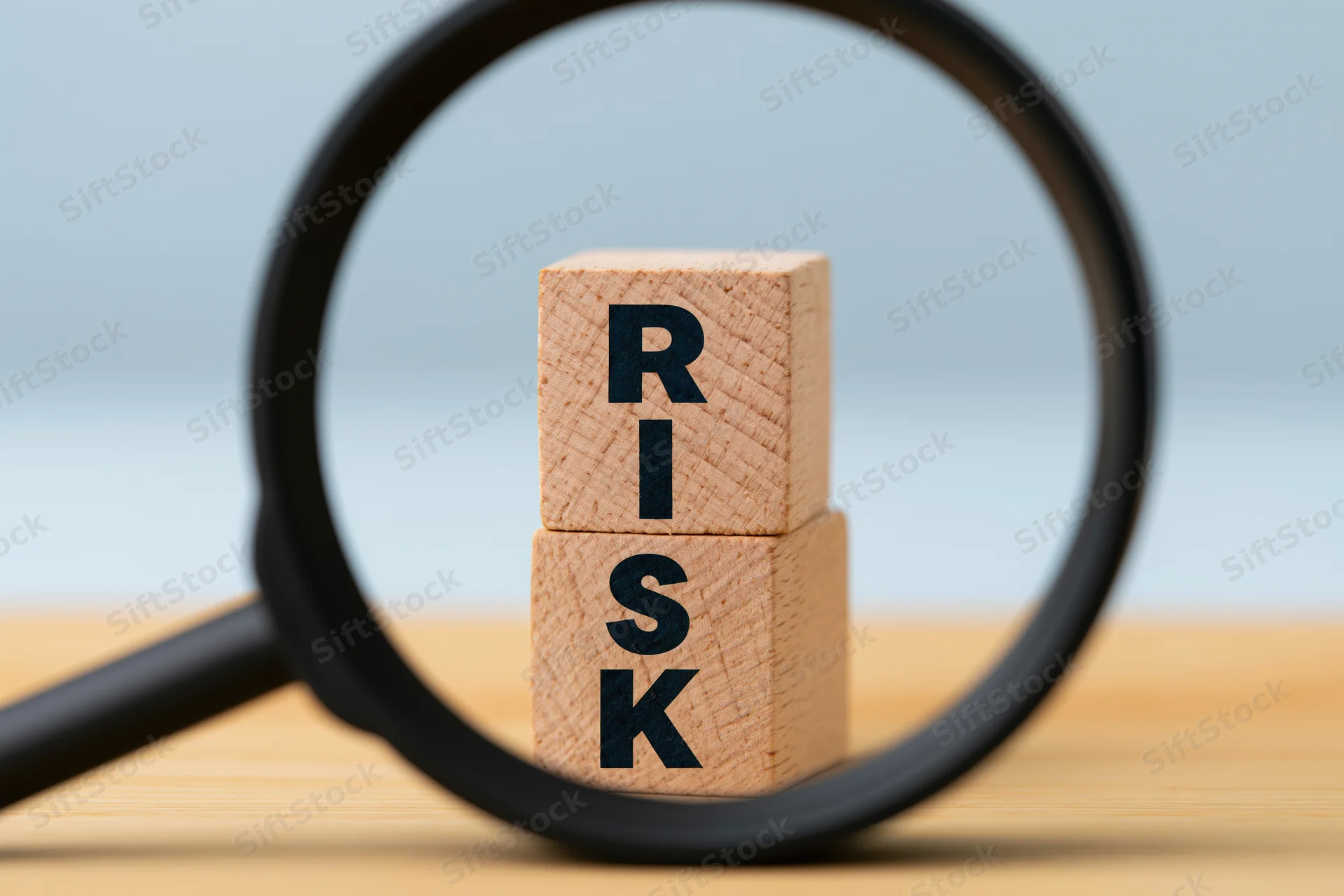Magnifying glass over stacked wooden blocks spelling risk on a desk