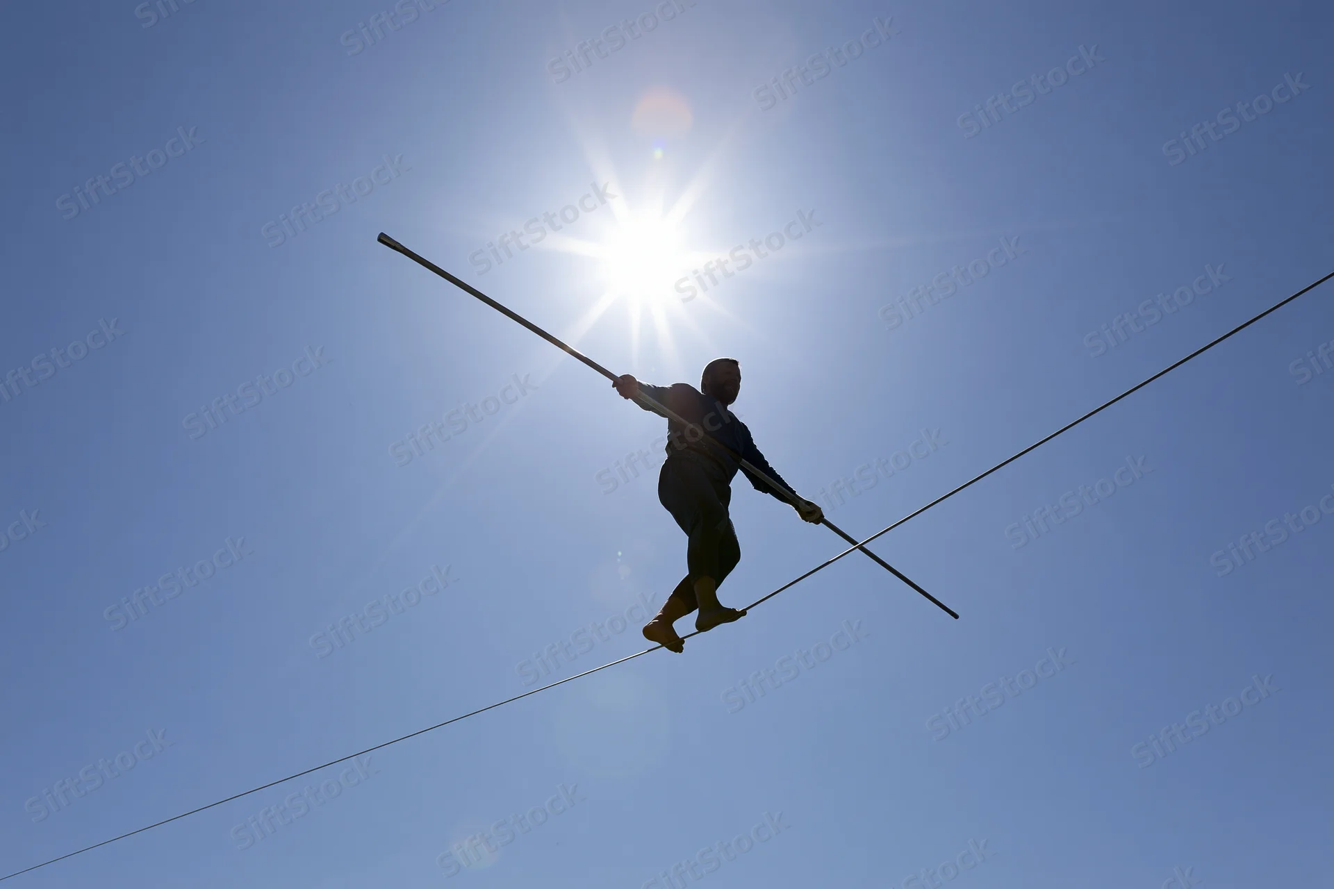 Tightrope walker balancing on high wire against bright midday sun