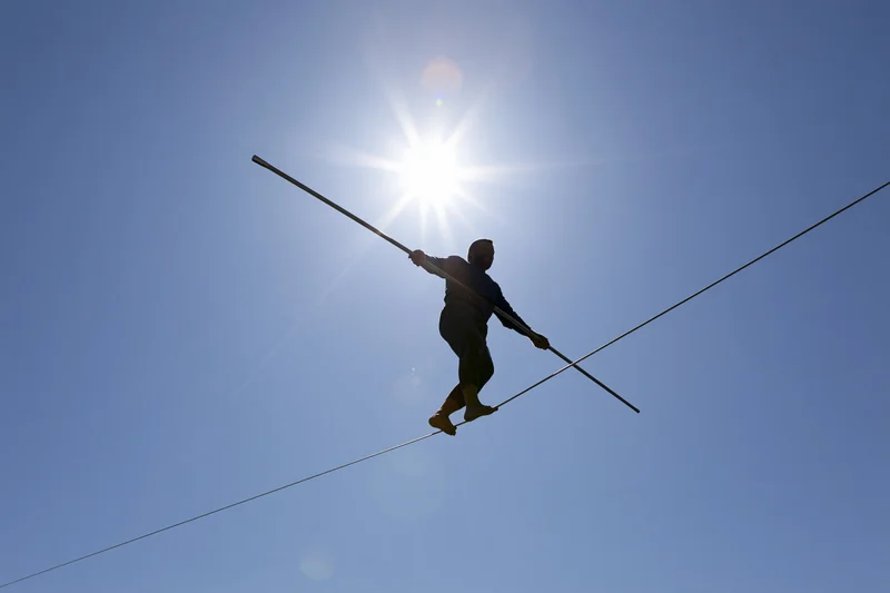 Tightrope walker balancing on high wire against bright midday sun