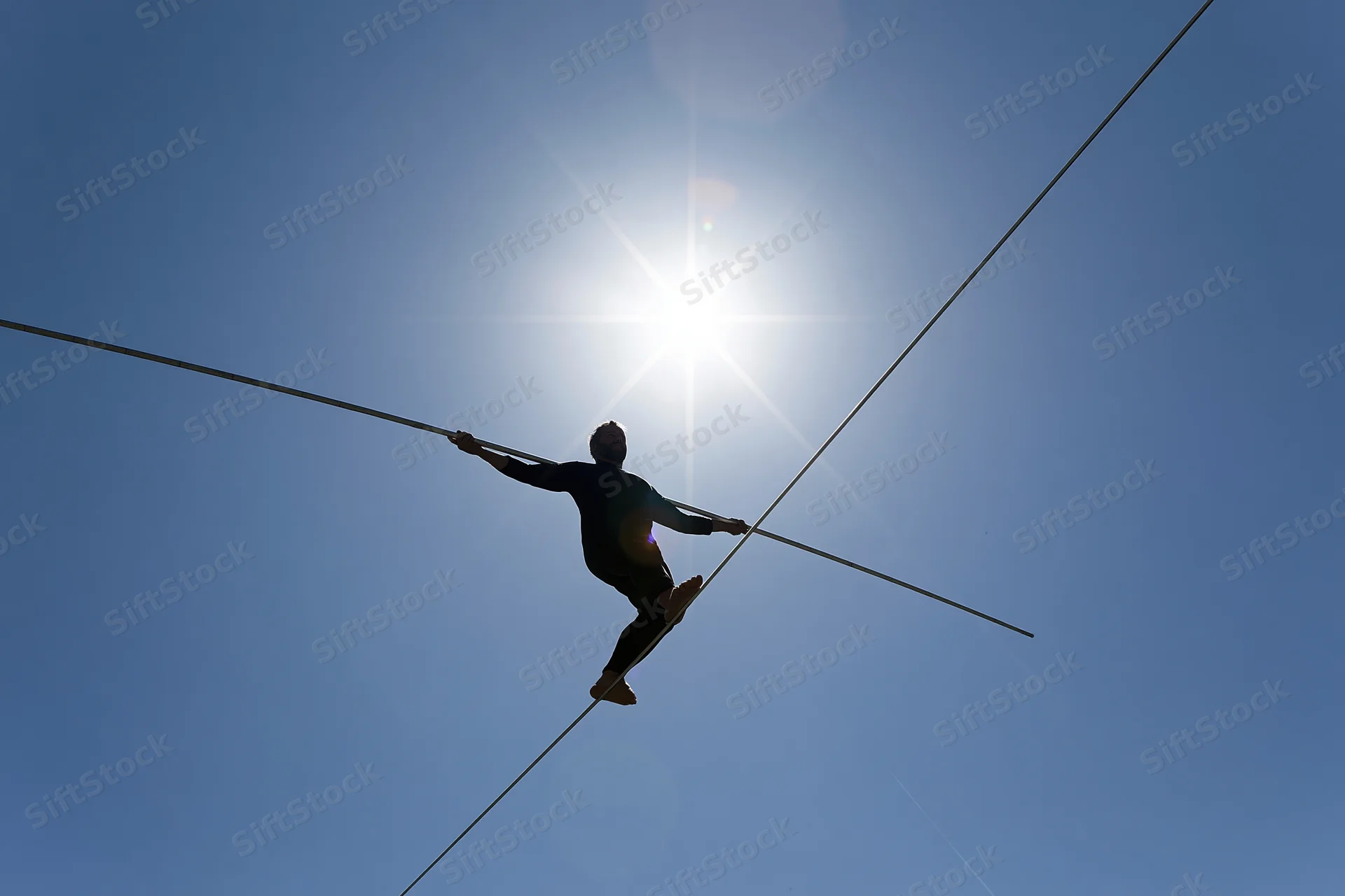 Tightrope walker balancing on a high wire against a bright midday sun