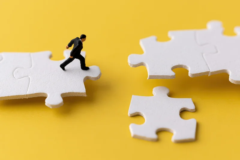 Miniature businessman figurine walking on puzzle pieces against yellow background