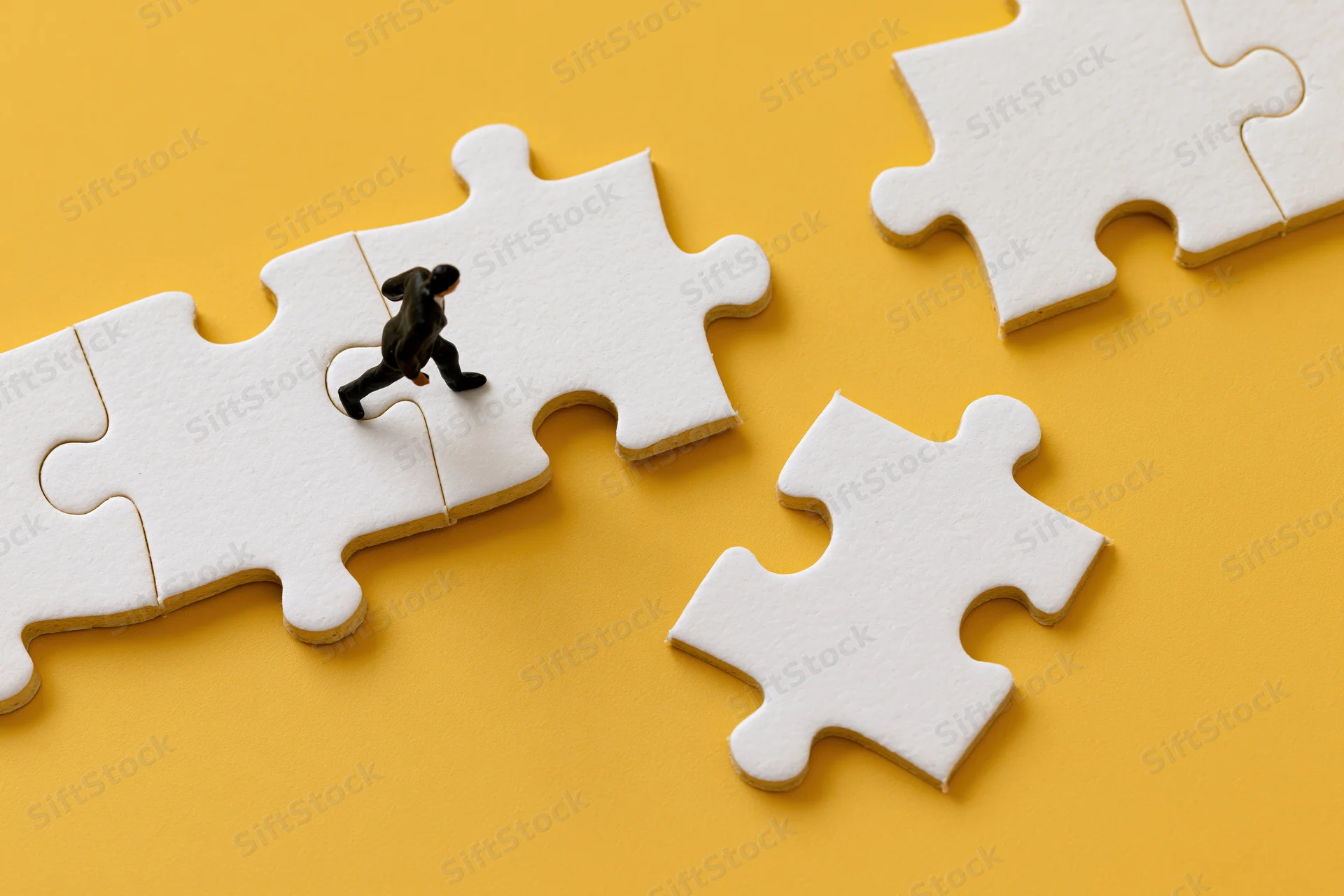 Miniature businessman figurine walking across white puzzle pieces on yellow background