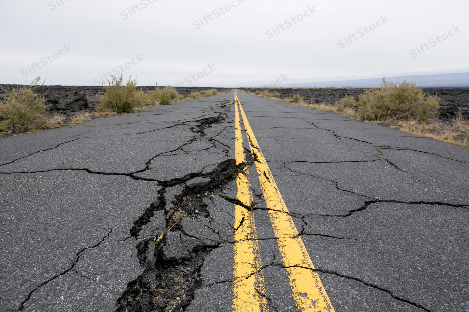 Cracked asphalt road with yellow center line stretching into the distance through volcanic terrain