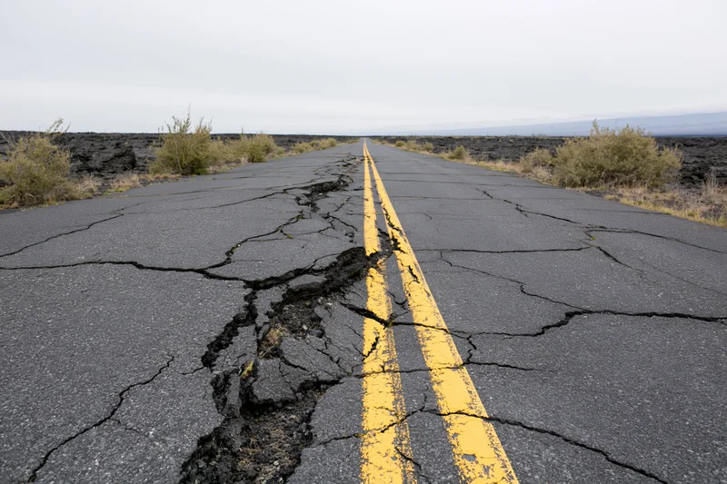 Cracked asphalt road with yellow center line stretching into the distance through volcanic terrain