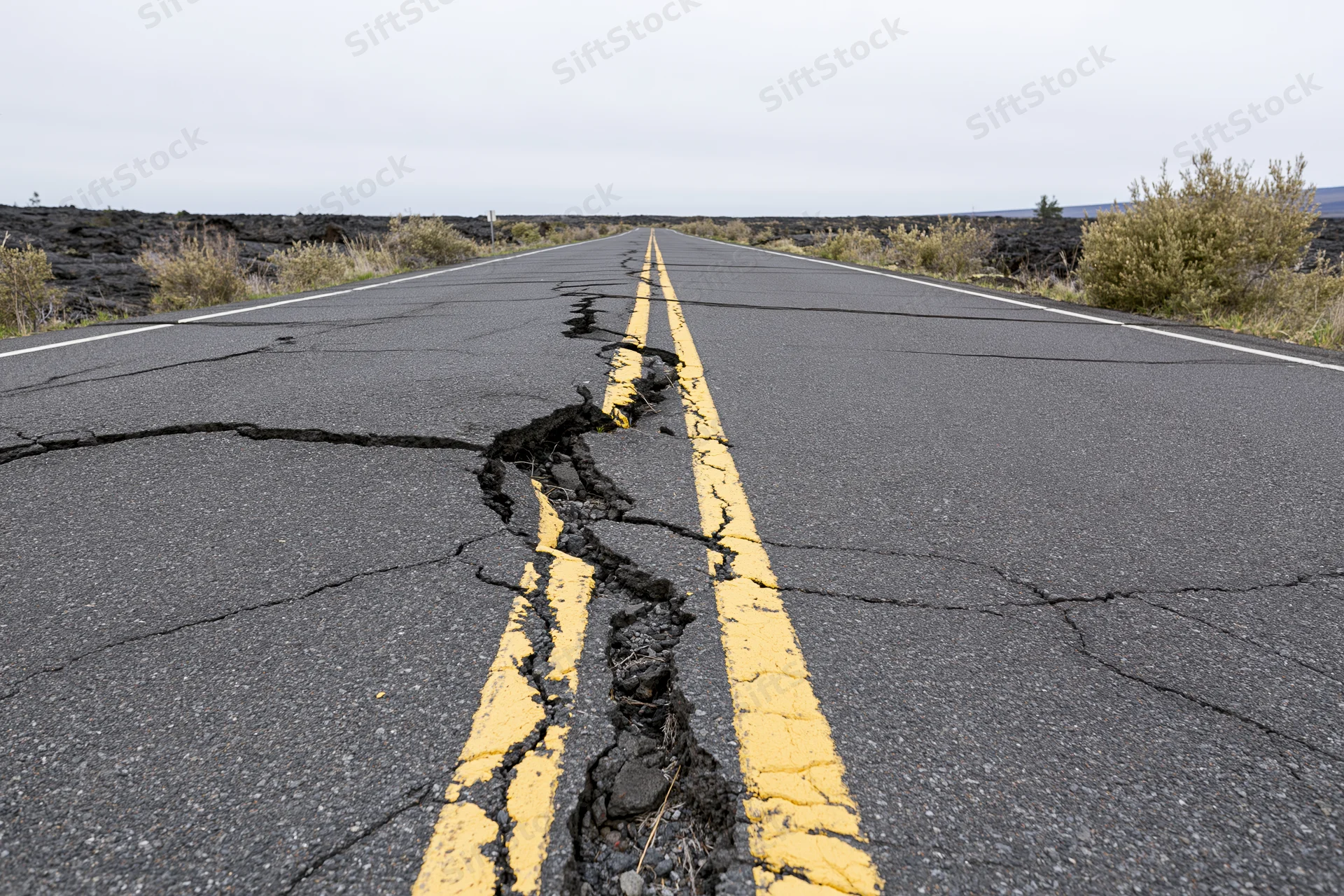 Cracked asphalt road with broken yellow center line running through volcanic landscape