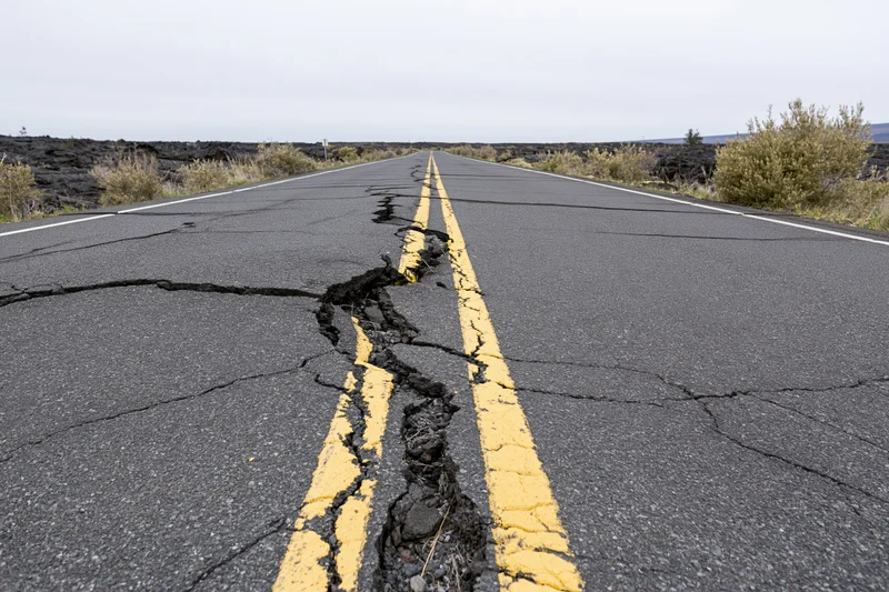 Cracked asphalt road with broken yellow center line running through volcanic landscape