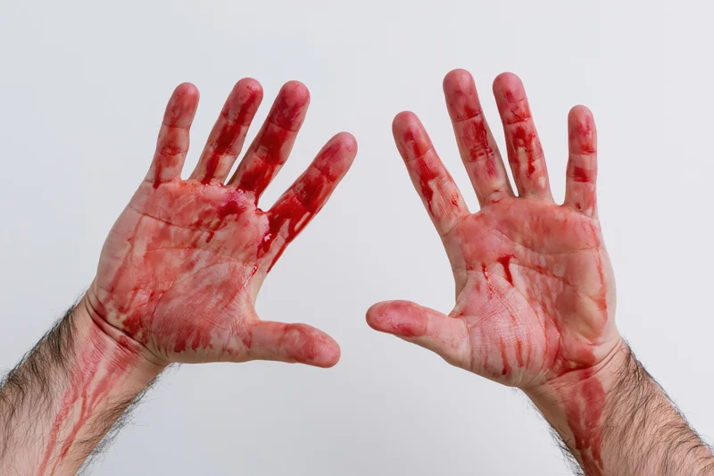 Two adult male hands raised palms forward covered in blood against white background
