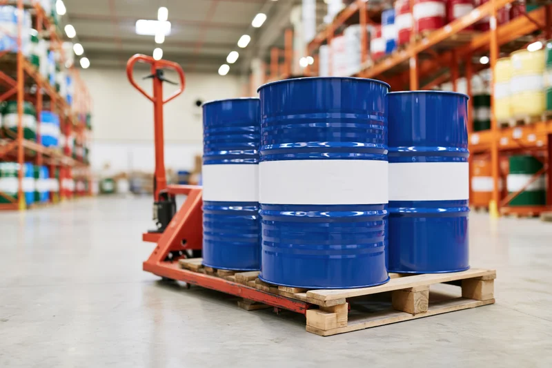 Blue metal industrial drums on wooden pallet in warehouse aisle with forklift and shelving in background