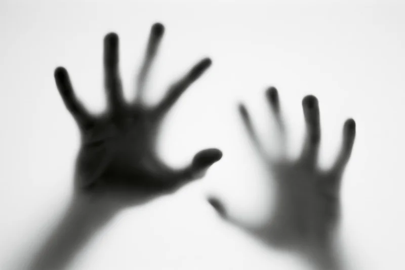 Blurred hands pressing against frosted glass in a white space