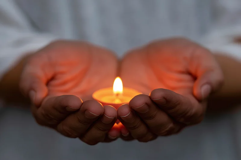 Cupped hands holding a small lit candle in a close-up view